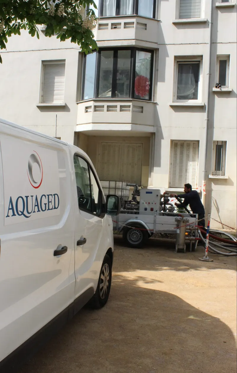 Technicien Aquaged raccordant un skid de désembouage au pied d’un immeuble